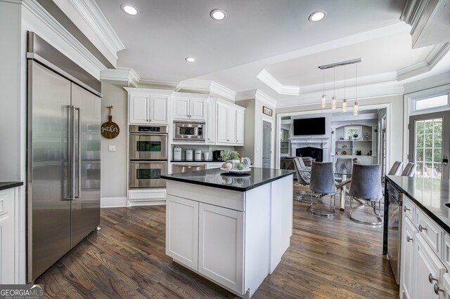 kitchen with built in appliances, a raised ceiling, dark hardwood / wood-style flooring, hanging light fixtures, and white cabinetry