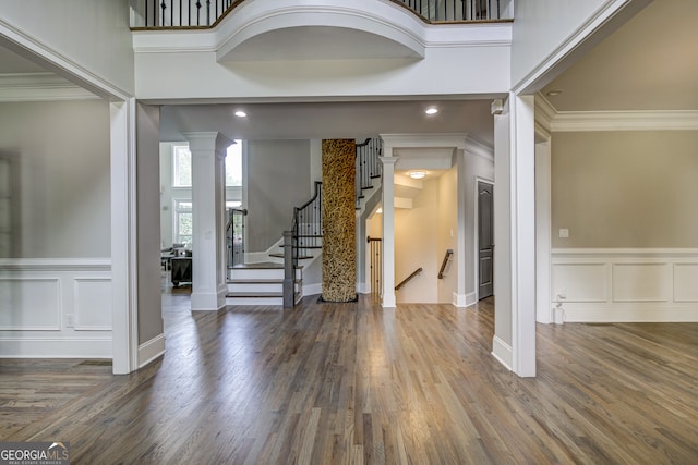 foyer entrance featuring crown molding, dark wood-type flooring, ornate columns, and a high ceiling