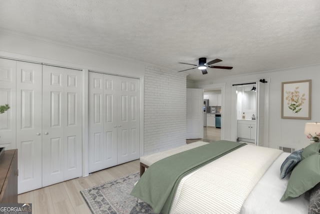 bedroom featuring light wood-type flooring, a textured ceiling, connected bathroom, and multiple closets