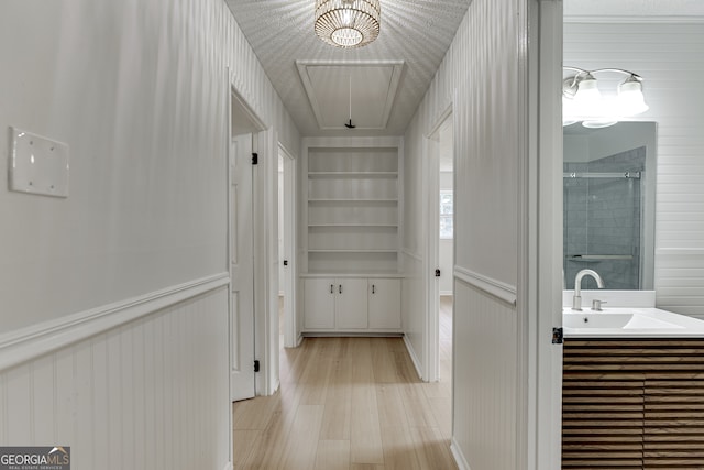 hall with a textured ceiling, built in shelves, sink, and light hardwood / wood-style flooring