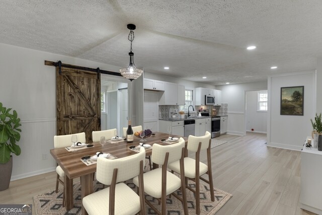 dining area with a barn door, sink, a textured ceiling, and light wood-type flooring