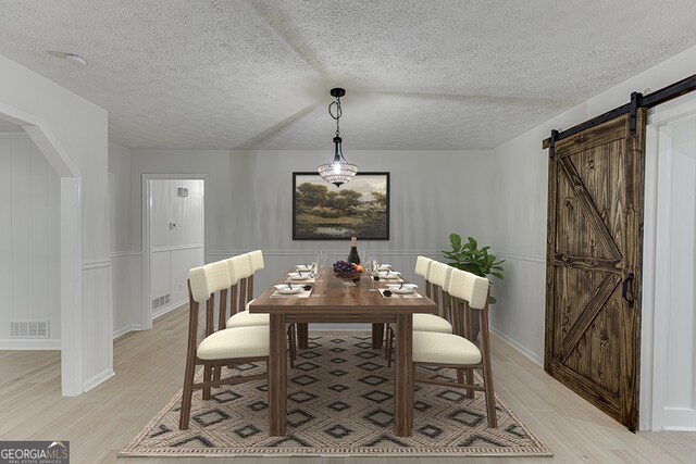 dining area with a barn door, light hardwood / wood-style floors, and a textured ceiling