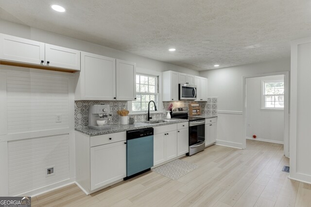 kitchen with white cabinets, stainless steel appliances, light stone counters, and sink