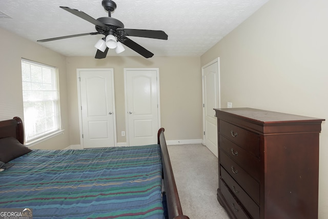 carpeted bedroom featuring a textured ceiling, ceiling fan, and two closets