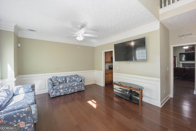 living room featuring dark wood-type flooring, ceiling fan, crown molding, and a textured ceiling