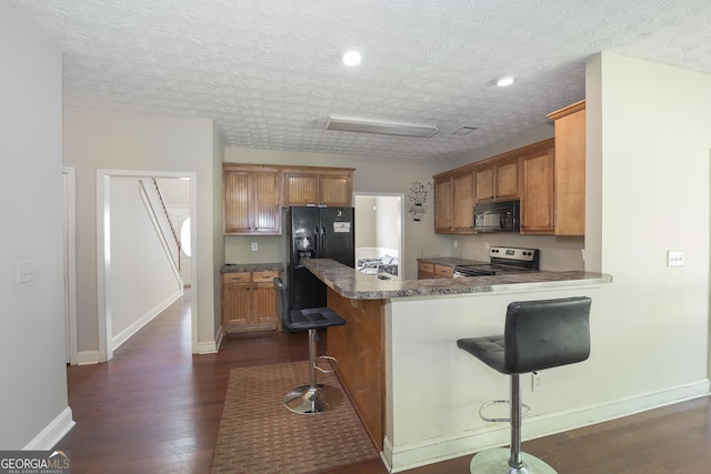 kitchen featuring black appliances, dark hardwood / wood-style flooring, kitchen peninsula, and a breakfast bar