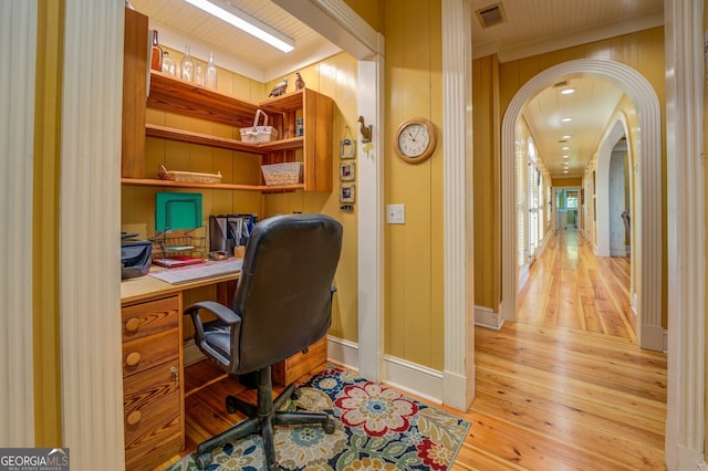 office space with built in desk, wooden walls, and light hardwood / wood-style floors