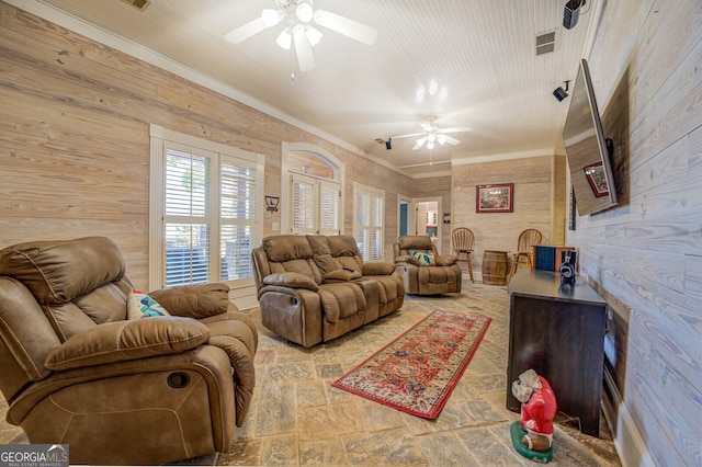 living room featuring wood walls, ceiling fan, and crown molding