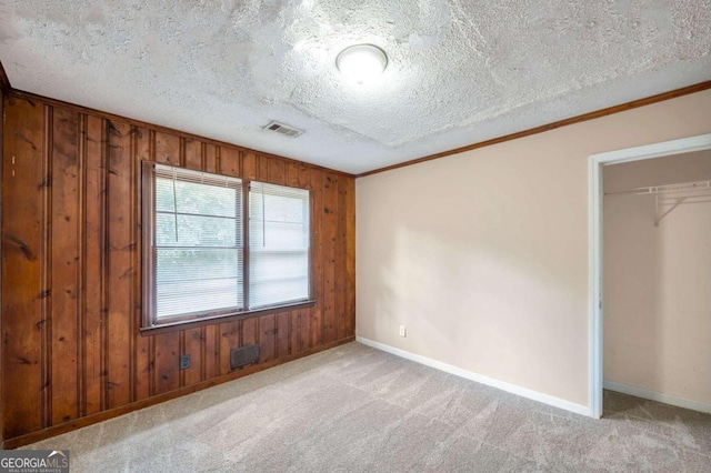 carpeted empty room featuring wood walls, crown molding, and a textured ceiling