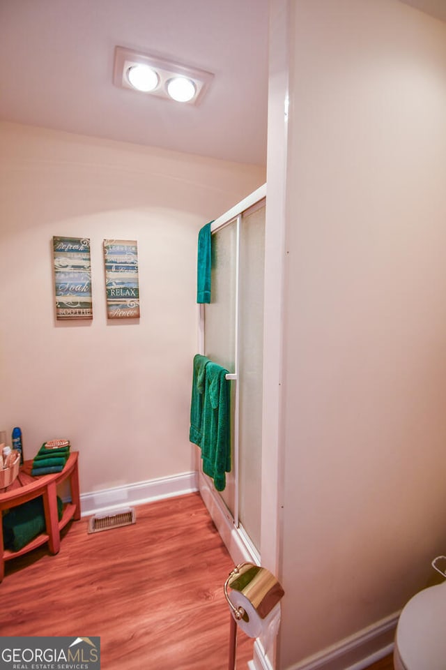 bathroom featuring toilet, wood-type flooring, and a shower with shower door