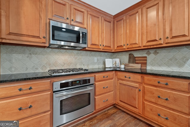 kitchen featuring stainless steel appliances, dark stone countertops, decorative backsplash, and dark hardwood / wood-style flooring