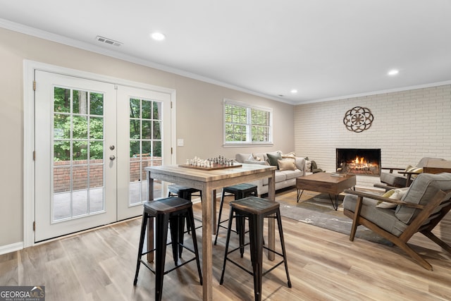 dining space featuring light hardwood / wood-style floors, ornamental molding, french doors, and a fireplace