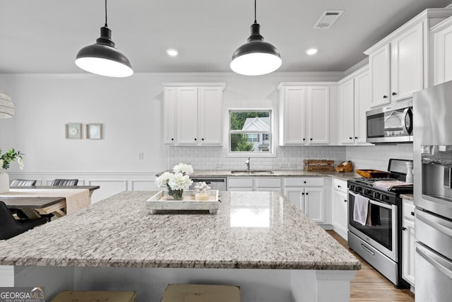 kitchen featuring appliances with stainless steel finishes, hanging light fixtures, sink, and white cabinets