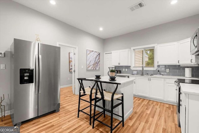 kitchen with white cabinetry, light hardwood / wood-style flooring, backsplash, a kitchen bar, and appliances with stainless steel finishes