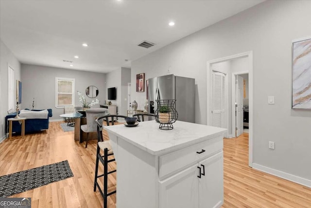 kitchen featuring white cabinets, a center island, light hardwood / wood-style floors, stainless steel fridge, and a breakfast bar