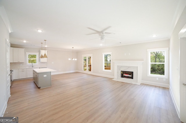 unfurnished living room featuring ceiling fan with notable chandelier, sink, light wood-type flooring, a fireplace, and ornamental molding