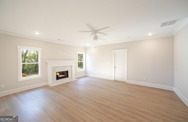 unfurnished living room featuring a premium fireplace, light hardwood / wood-style flooring, ceiling fan, and crown molding