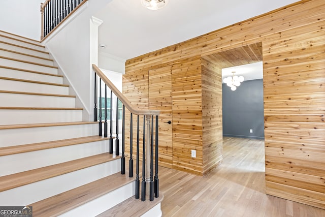 stairway with wood-type flooring, wood walls, and a chandelier