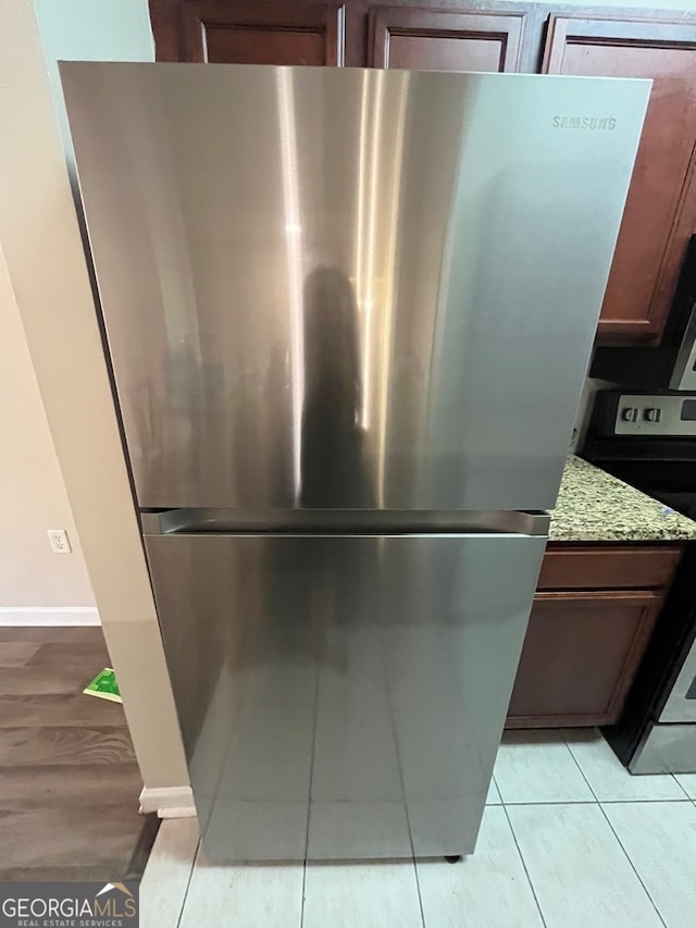 details with light tile patterned floors, appliances with stainless steel finishes, light stone counters, and dark brown cabinetry