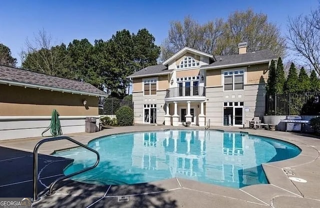 rear view of house with a fenced in pool, a patio area, and a balcony