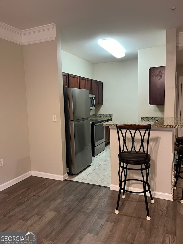 kitchen featuring light wood-type flooring, crown molding, kitchen peninsula, appliances with stainless steel finishes, and a breakfast bar area