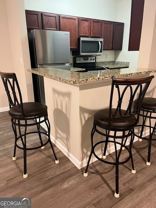 kitchen featuring hardwood / wood-style floors, light stone countertops, black range with electric stovetop, kitchen peninsula, and a kitchen breakfast bar