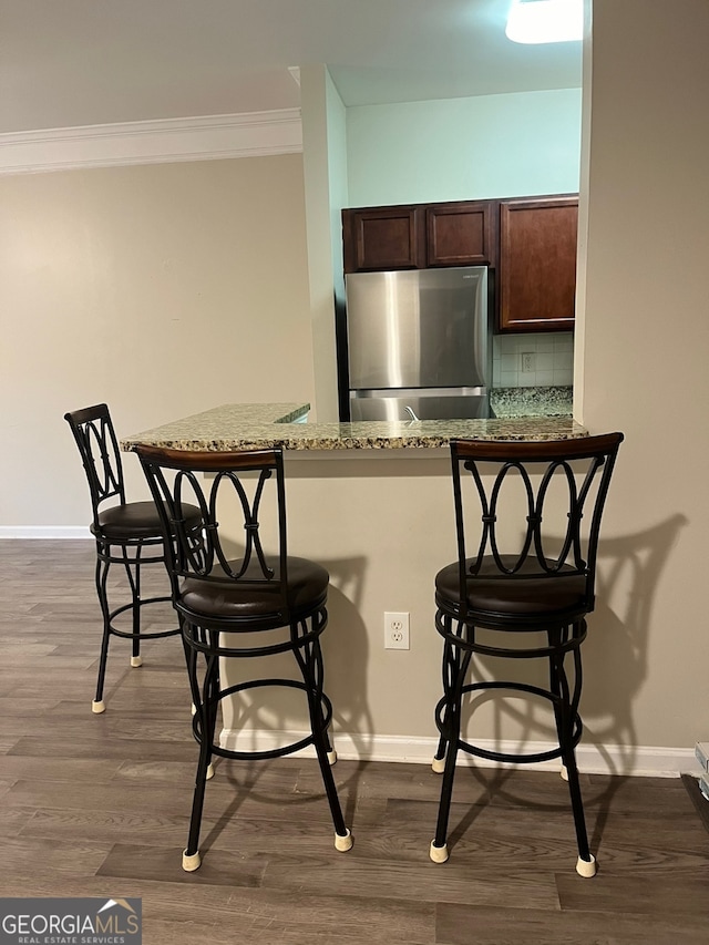 kitchen featuring crown molding, light stone countertops, dark hardwood / wood-style flooring, stainless steel fridge, and a kitchen breakfast bar