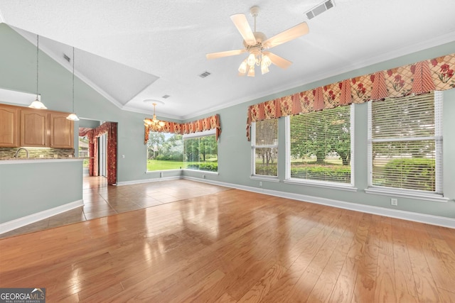 unfurnished living room featuring ceiling fan with notable chandelier, a textured ceiling, crown molding, lofted ceiling, and light hardwood / wood-style flooring