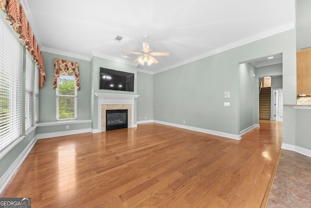 unfurnished living room featuring ceiling fan, light hardwood / wood-style flooring, a tiled fireplace, and crown molding