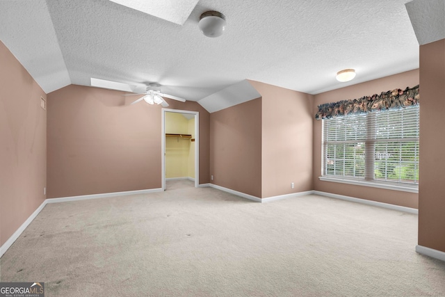 spare room with vaulted ceiling with skylight, ceiling fan, carpet flooring, and a textured ceiling