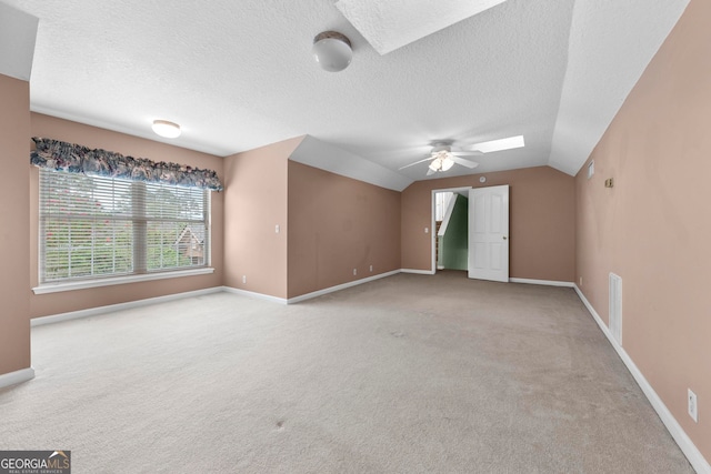 carpeted empty room featuring ceiling fan, a textured ceiling, and lofted ceiling with skylight