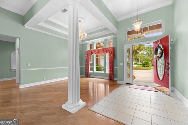 entrance foyer featuring a chandelier, a tray ceiling, decorative columns, light wood-type flooring, and crown molding