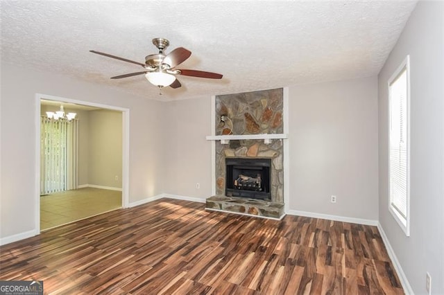 unfurnished living room featuring ceiling fan with notable chandelier, a textured ceiling, dark hardwood / wood-style floors, and a stone fireplace