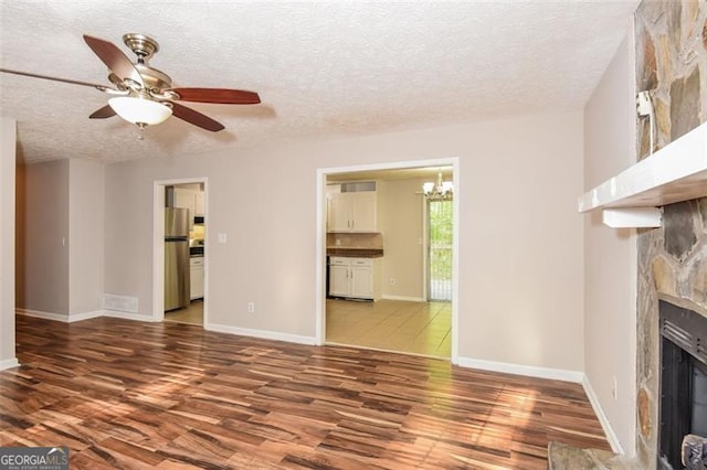 unfurnished living room featuring a textured ceiling, ceiling fan with notable chandelier, hardwood / wood-style flooring, and a fireplace