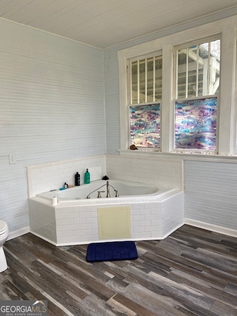 bathroom with wood-type flooring, toilet, and tiled bath