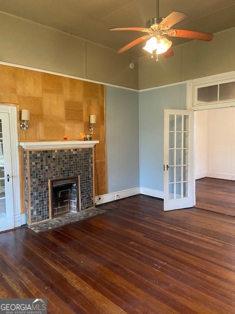 unfurnished living room featuring a towering ceiling, ceiling fan, a tiled fireplace, and dark hardwood / wood-style flooring