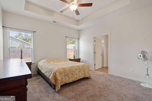 carpeted bedroom with ceiling fan and a tray ceiling