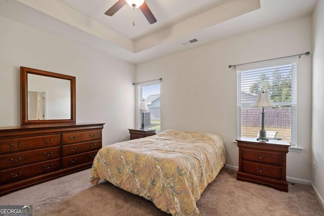 bedroom with light colored carpet, a raised ceiling, and ceiling fan