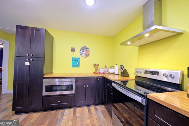 kitchen featuring dark brown cabinets, wood counters, extractor fan, stainless steel appliances, and light wood-type flooring