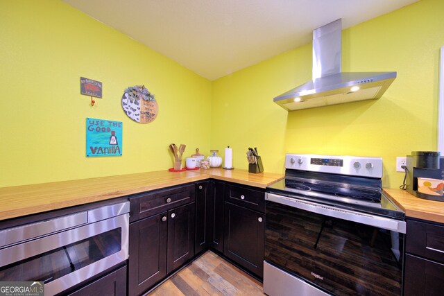 kitchen featuring butcher block countertops, light hardwood / wood-style flooring, stainless steel appliances, and wall chimney range hood