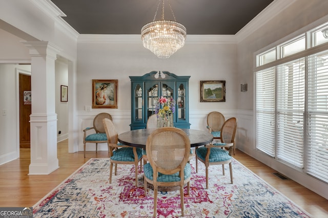 dining area featuring a notable chandelier, decorative columns, crown molding, and light hardwood / wood-style flooring