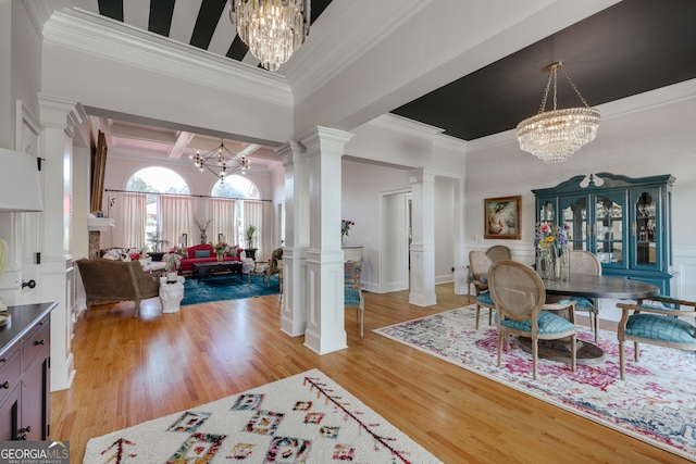 foyer entrance featuring crown molding, a chandelier, decorative columns, and light hardwood / wood-style floors