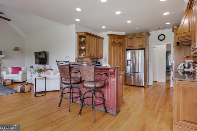 kitchen with light wood-type flooring, a kitchen bar, ceiling fan, stainless steel fridge with ice dispenser, and vaulted ceiling