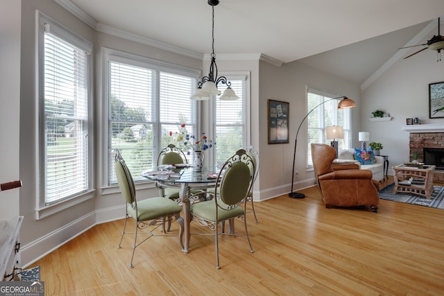 dining space featuring a fireplace, vaulted ceiling, light hardwood / wood-style flooring, ceiling fan with notable chandelier, and ornamental molding