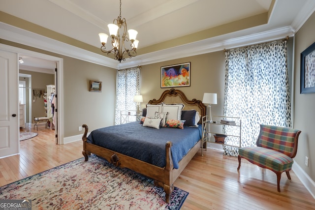 bedroom with a raised ceiling, ornamental molding, a chandelier, and light hardwood / wood-style floors