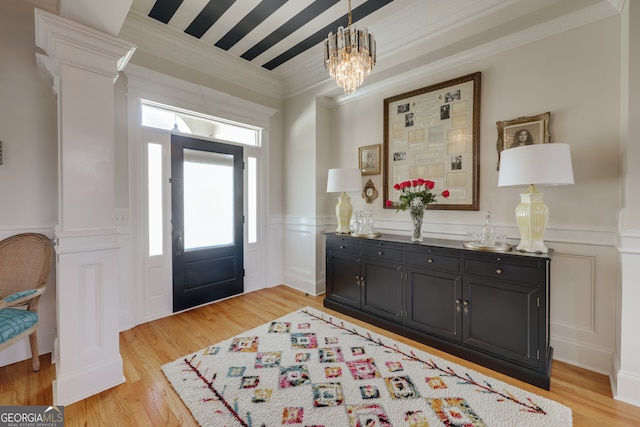 foyer with crown molding, ornate columns, an inviting chandelier, and light hardwood / wood-style floors