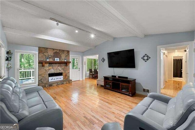 living room with baseboards, lofted ceiling with beams, wood finished floors, a fireplace, and track lighting