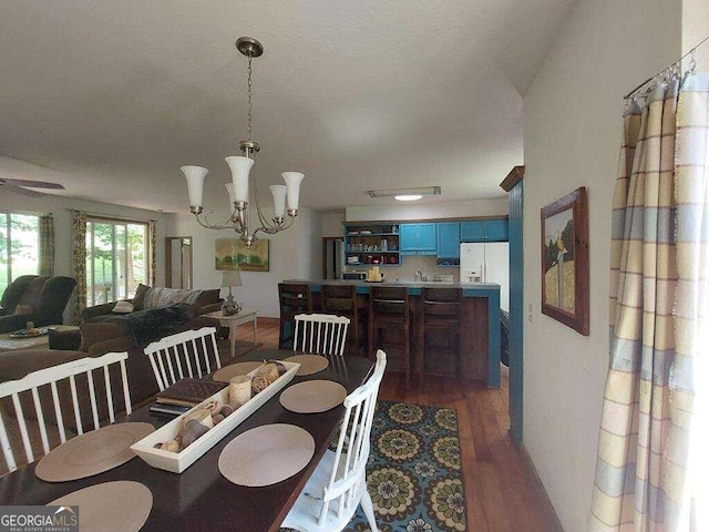 dining space with dark wood-type flooring, vaulted ceiling, and a notable chandelier