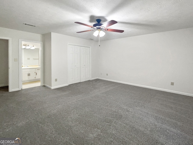 unfurnished bedroom featuring a textured ceiling, connected bathroom, ceiling fan, a closet, and dark colored carpet