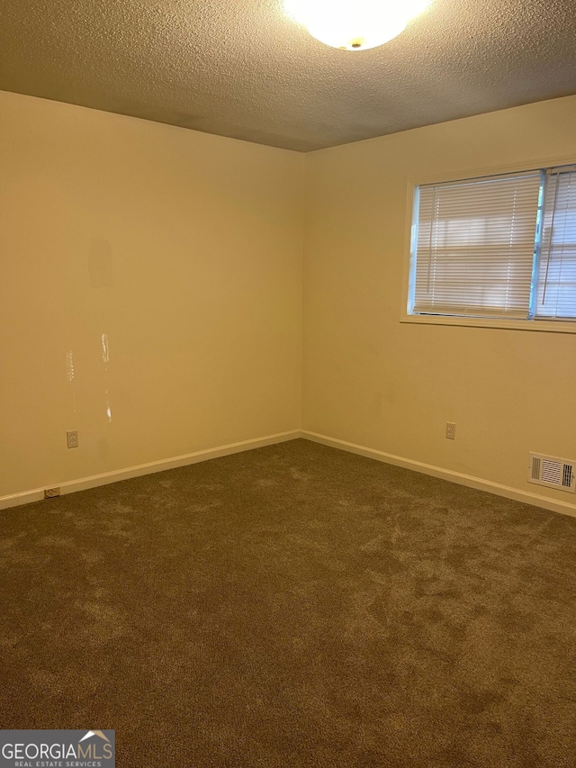 spare room featuring dark carpet and a textured ceiling